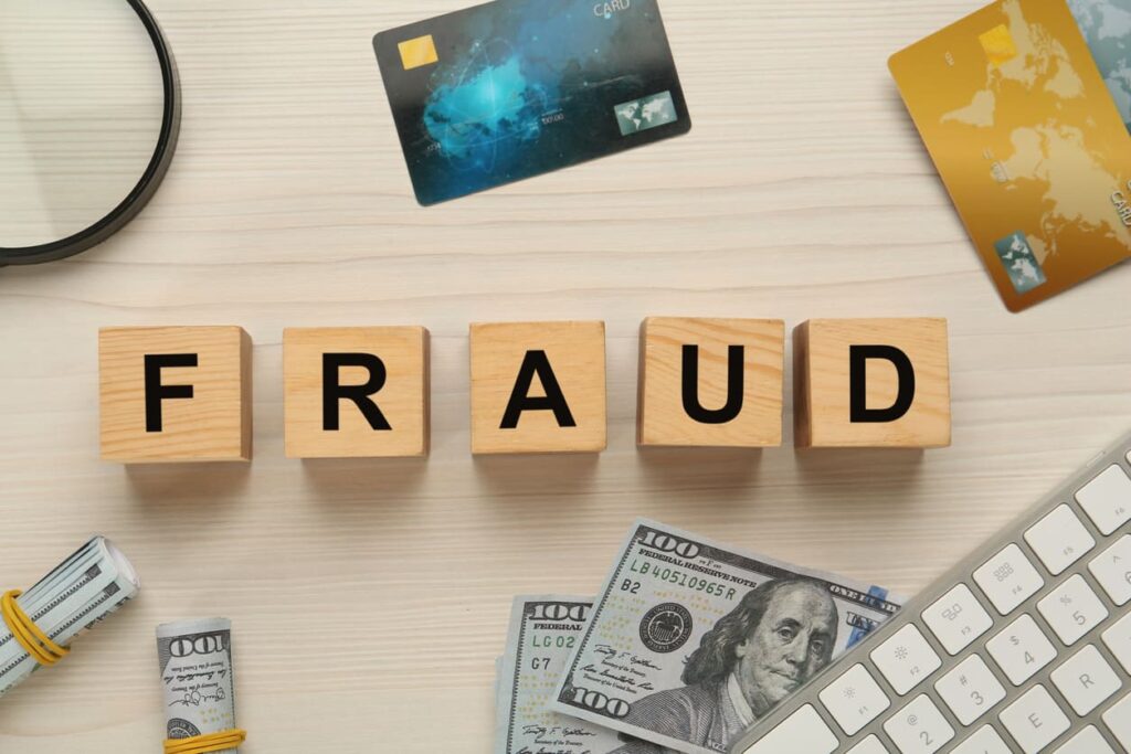 Fraud concept with wooden blocks spelling FRAUD, credit cards, cash, magnifying glass, and keyboard on desk.