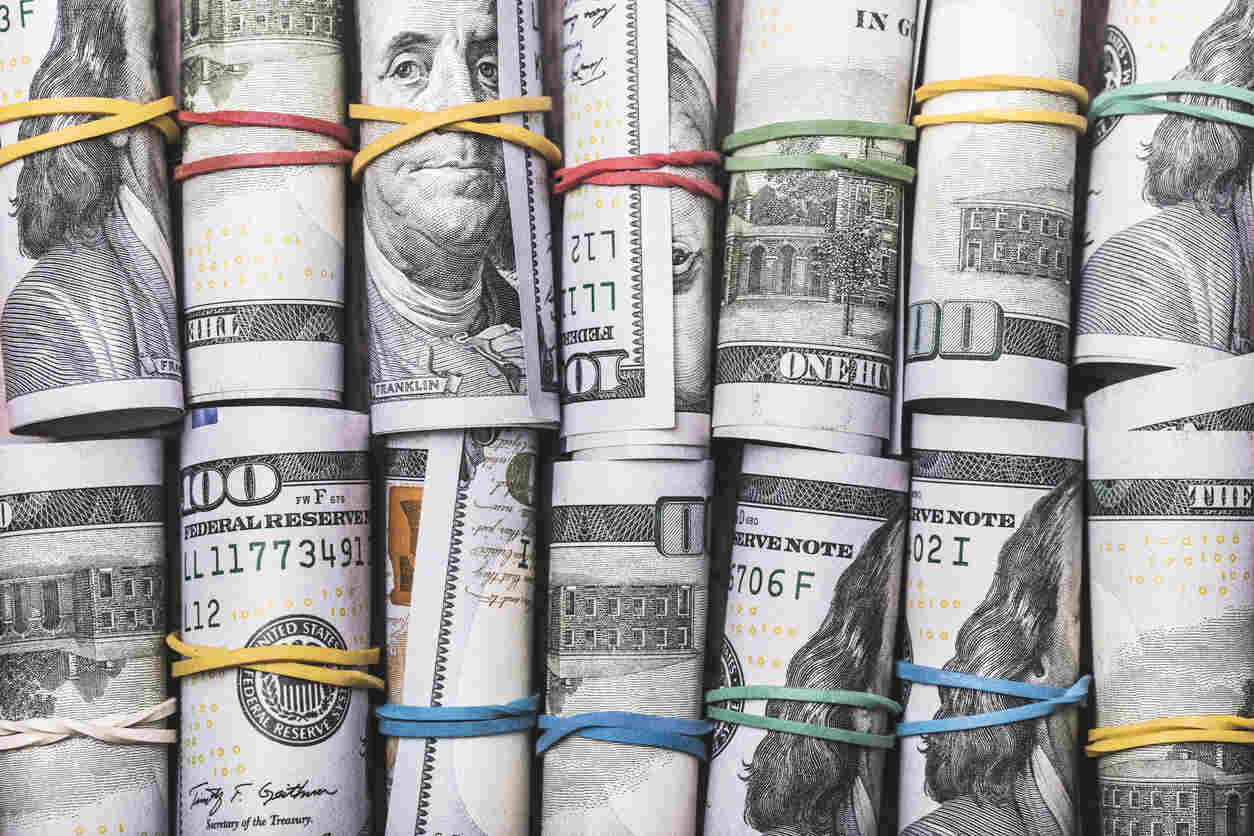 A close-up shot of several stacks of rolled-up hundred-dollar bills, held together by rubber bands. This image represents the financial assets involved in money laundering and highlights the risks of federal investigations for financial institutions and clients.
