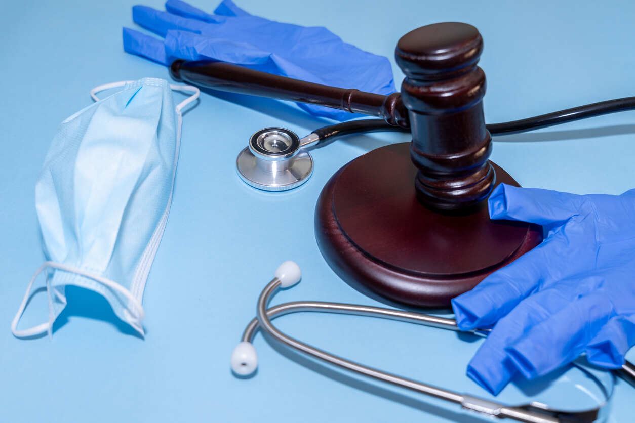 Gavel, medical mask, and stethoscope on a blue background, symbolizing the intersection of legal and medical issues in parallel civil and criminal investigations, with potential hidden risks for professionals